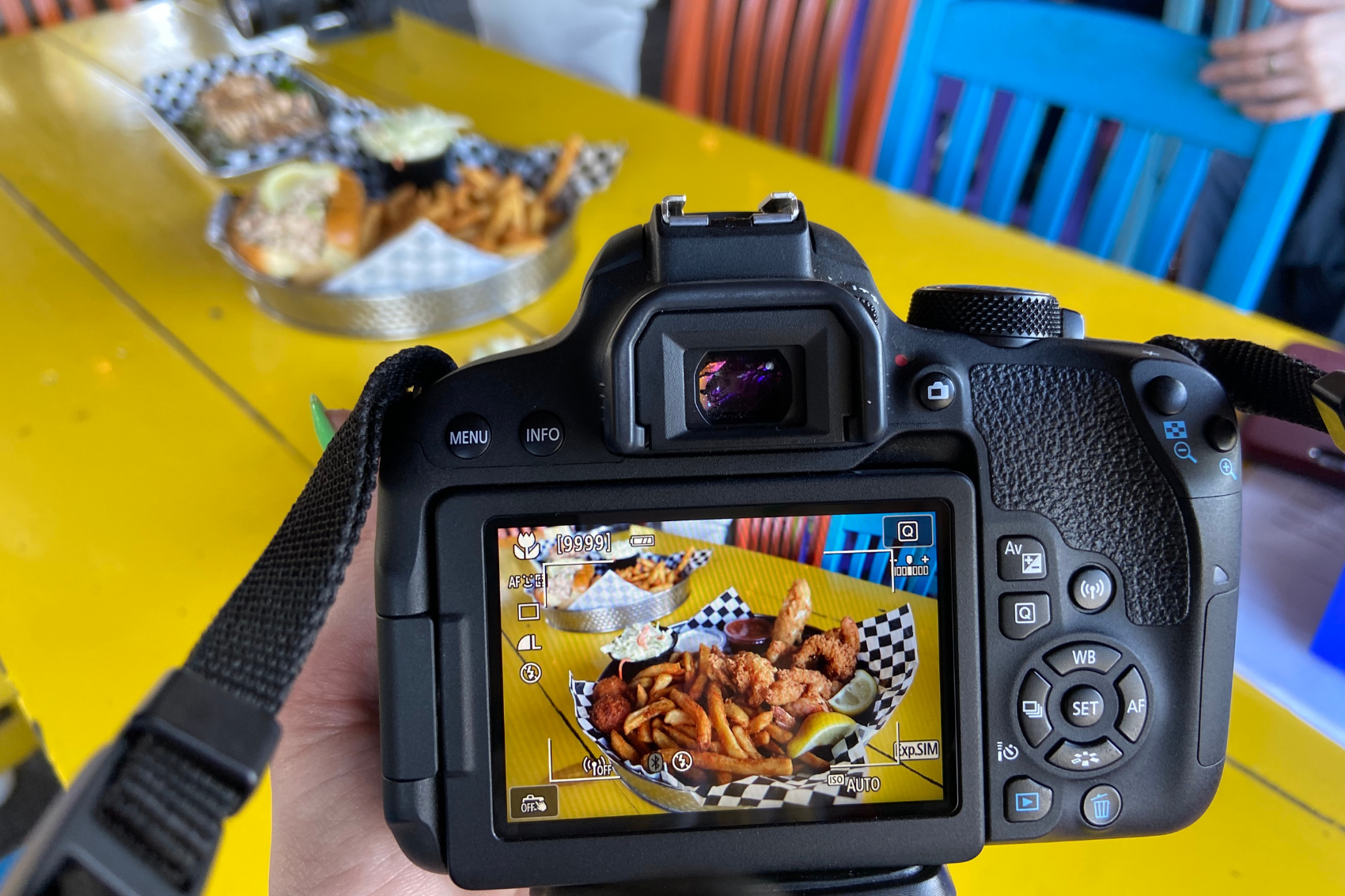 A camera taking a picture of fish and chips on a yellow table.